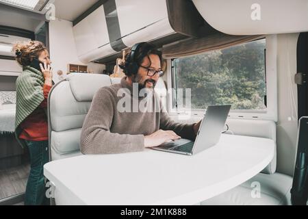 Camper van tourists vacation real scene lifestyle. Man and woman enjoying motor home alternative house interior. One working at the laptop and wife sp Stock Photo