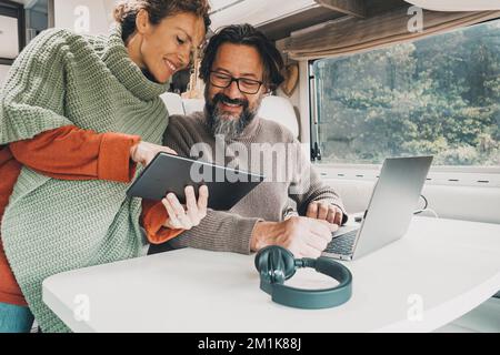 Modern couple of traveler enjoy work office inside camper van. Happy woman and man in modern job activity with freedom of motor home vehicle. Alternat Stock Photo