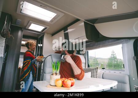 Camper van indoor leisure activity and lifestyle with woman cooking and man looking and talking to her. Happy couple on vacation with motor home. Alte Stock Photo