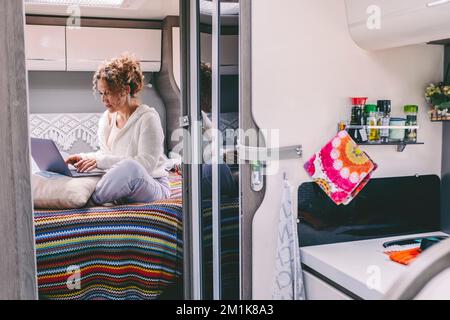 Alternative office workplace concept. Woman working on laptop in camper van bedroom. Van life and smart travel working life. Female people in modern j Stock Photo