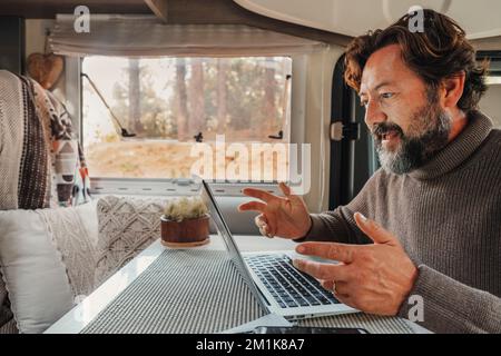 Video call conference in freedom office workplace lifestyle. One man speaking with internet and laptop inside a camper van parked in the nature park.. Stock Photo