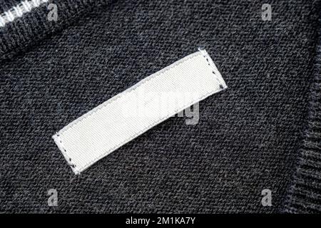 White blank label, patch or tag with space for text  on knitted gray sweater, top view Stock Photo