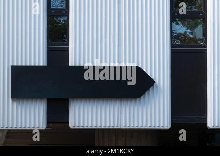 Mock up. Blank black arrow shape signboard on the wall outdoors. Signage of office, shop, store, cafe, restaurant Stock Photo
