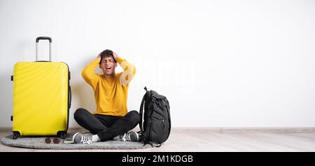 Sick traveler with headache sitting with suitcase over isolated white background having migraine and health problems. Banner Stock Photo