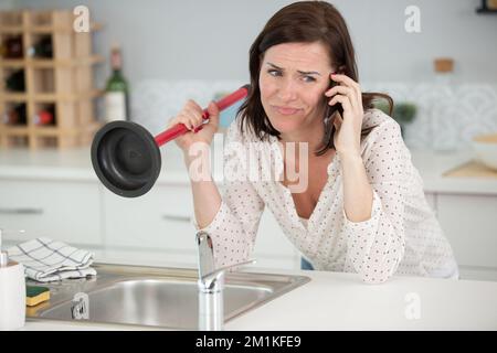 https://l450v.alamy.com/450v/2m1kfe9/woman-using-plunger-in-kitchen-sink-calling-a-plumber-2m1kfe9.jpg