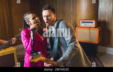 Vocalist and guitarist. Indoor portrait of caucasian woman singer singing to the microphone with male guitarist during a concert. High quality photo Stock Photo