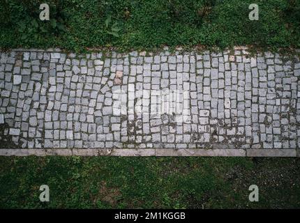 Horizontal pavement stone road with green grass top view. Stock Photo
