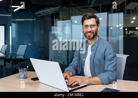 Portrait of mature businessman inside modern office, senior man in shirt smiling and looking at camera, worker using laptop at work. Stock Photo