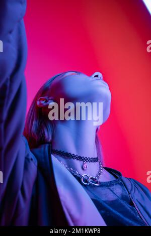 low angle view of woman in necklaces posing in blue neon light on coral background,stock image Stock Photo