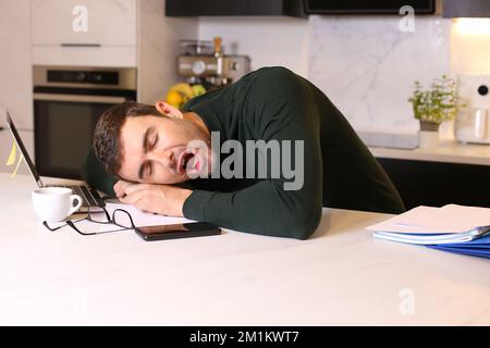 Man falling sleep while working remotely from his kitchen Stock Photo