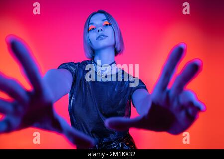 low angle view of woman with glowing makeup and outstretched hands in blue neon light on coral and pink background,stock image Stock Photo