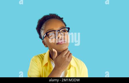 Portrait of pensive woman who has doubtful expression on her face against light blue background. Stock Photo