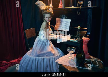 Emotive young girl in image of medieval person in elegant white dress writing music composition with thoughtful face. Melody making. Comparison of Stock Photo
