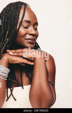 Elegant woman with dreadlocks wearing a bath towel and light make-up in a studio. Mature woman standing against a white background with her eyes close Stock Photo