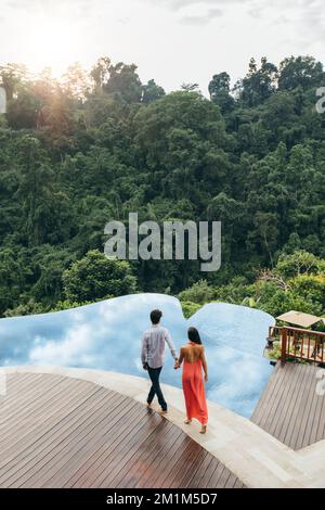 Aerial shot of young couple walking towards pool at luxury resort. Man and woman holding hands near swimming pool. Stock Photo