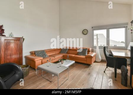 a living room with wood flooring and an orange leather couch in the center of the room is a dining table Stock Photo