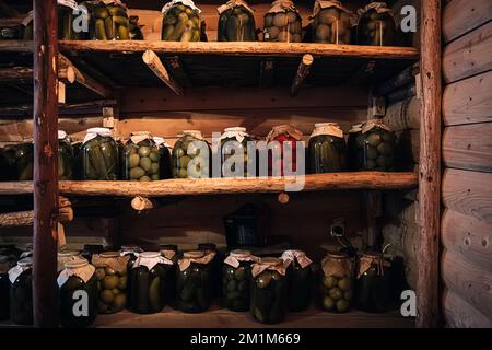 Preservation of vegetables in a warm cellar for the winter period. Glass jars with pickled cucumbers on the shelf. Stock Photo