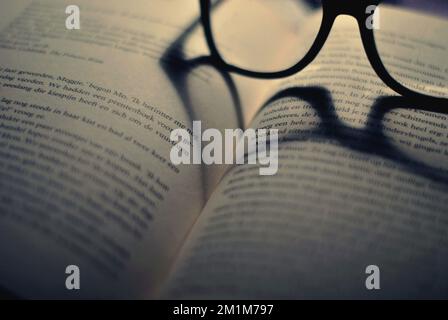 Glasses placed on a book so that the shadow creates a heart Stock Photo