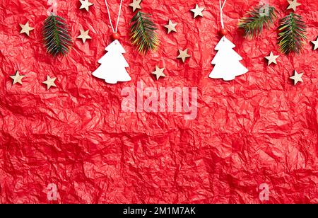 Red crumpled silk paper background with Christmas decorations on upper section, lot of copy space. Studio shot. White Christmas tree shape ornaments. Stock Photo