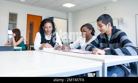 College Class: Working With Teacher. A pair of late teenage students working with their teacher in the classroom. From a series of related images. Stock Photo