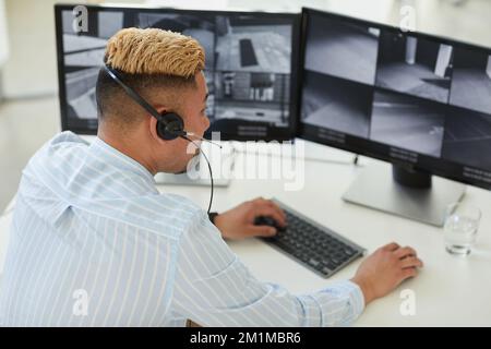 High angle view at Asian man wearing headset looking at multiple surveillance feeds in monitoring and security center Stock Photo