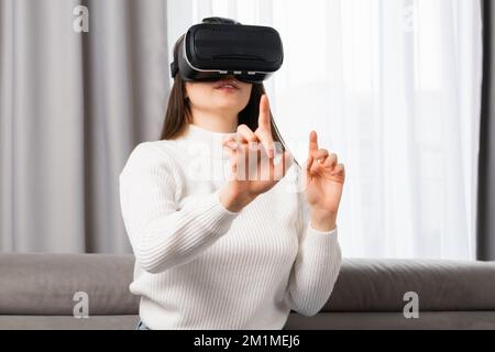 A beautiful teen girl interacts with virtual reality and touches an invisible interface sitting on the safe in the living room Stock Photo