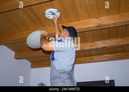 Image of an electrician who on a ladder replaces a burnt out light bulb with a LED one. Stock Photo