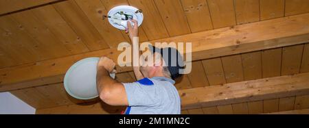 Image of an electrician who on a ladder replaces a burnt out light bulb with a LED one. Horizontal banner Stock Photo