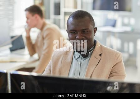 Portrait of smiling black man looking at computer screen while working in customer support and surveillance center Stock Photo