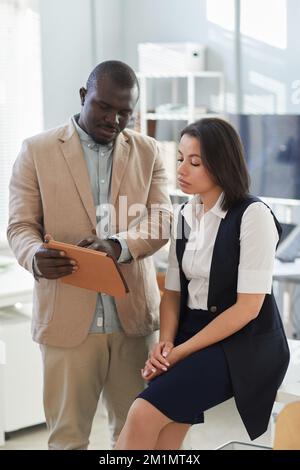 Vertical portrait of black businessman talking to female colleague in office and holding digital tablet Stock Photo