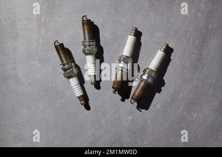 four dirty used car spark plugs on a grey floor Stock Photo