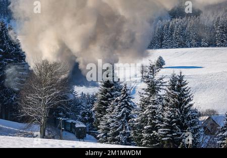 Cranzahl, Germany. 13th Dec, 2022. The Fichtelberg Railway makes its way through the snowy winter forest in the Ore Mountains with plenty of smoke and clouds of smoke. The narrow-gauge railroad is struggling with increased coal prices. The Sächsisches Dampfeisenbahngesellschaft mbH (SDG) needs around 800 tons of coal per year for the Fichtelberg, Lößnitzgrund and Weißeritztalbahn. To save money, it therefore now only operates one steam locomotive on the line. The other railroads are also thinning out operations at off-peak times. Credit: Jan Woitas/dpa/Alamy Live News Stock Photo