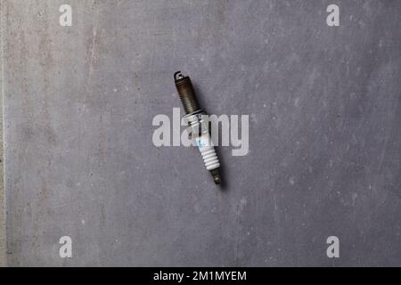 a dirty used spark plug on a grey floor Stock Photo