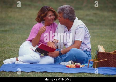 Middle aged couple outside having a picnic sitting on a blanket Stock Photo