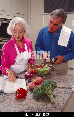 Older retired couple standing in kitchen preparing a meal together Stock Photo