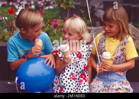 Boy and two girls sitting on a park bench eating ice cream Stock Photo