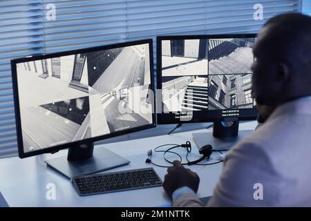 Back view black man looking at surveillance camera footage in security center, blue tones Stock Photo