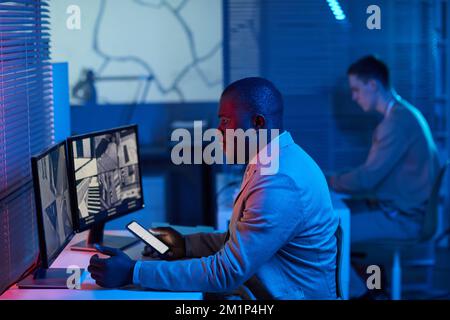 Futuristic side view portrait of black man looking at surveillance camera footage in security center office Stock Photo