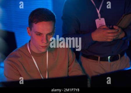 Portrait of young man looking at computer screen while working in data security center with blue and red tones Stock Photo