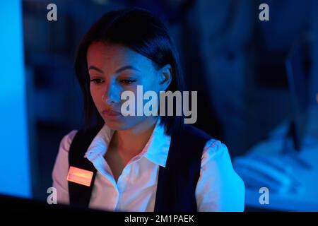 Close up of young woman watching surveillance camera feed in dark office Stock Photo
