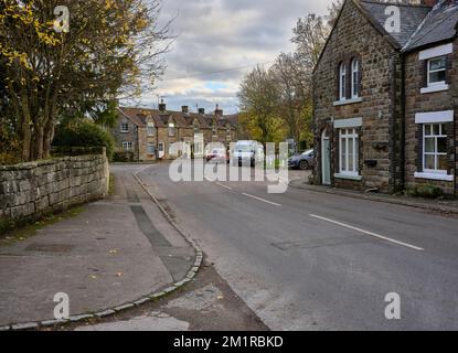 With the 'Graze on the Green' café ahead, late afternoon sun picks out the autumn colours on the road leading south into Rosedale Abbey.  North Yorks Stock Photo