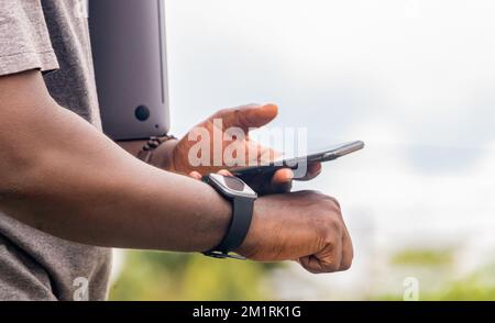 African black man pointing finger at smart phone in city , texting on mobile phone, sparkling street lifestyle, blurred background Stock Photo