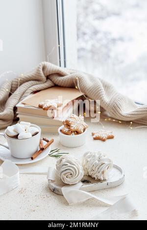 Cozy Christmas aesthetics background - white marshmallows, hot cocoa, ginger homemade cookies and books at home in snowy day outside. Aesthetics home. Stock Photo