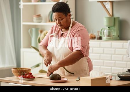 Warm toned portrait of black senior woman cooking in cozy home kitchen, copy space Stock Photo