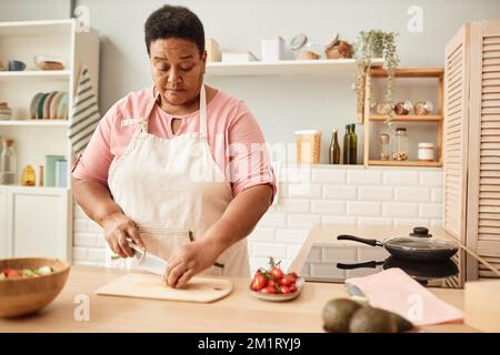 Warm toned waist up portrait of black senior woman cutting vegetables while making salad in cozy kitchen, copy space Stock Photo