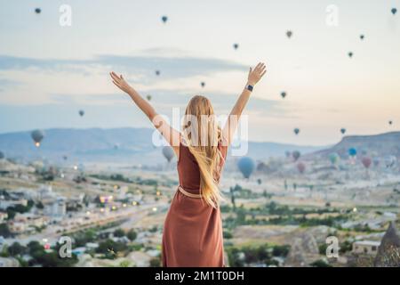 Tourist woman looking at hot air balloons in Cappadocia, Turkey. Happy Travel in Turkey concept. Woman on a mountain top enjoying wonderful view Stock Photo