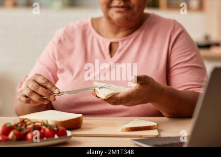 Close up of black woman making sandwich while enjoying breakfast in cozy kitchen, copy space Stock Photo