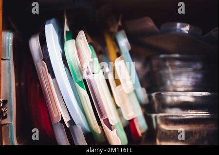Narrow depth of field picture of an open kitchen cabinet with an assortment of containers and mismatched lids stacked. Stock Photo