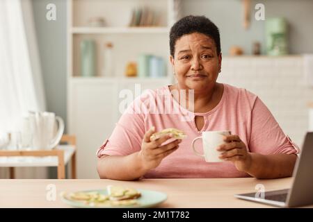Warm toned portrait of black senior woman enjoying cup of coffee during breakfast in morning and looking at camera, copy space Stock Photo
