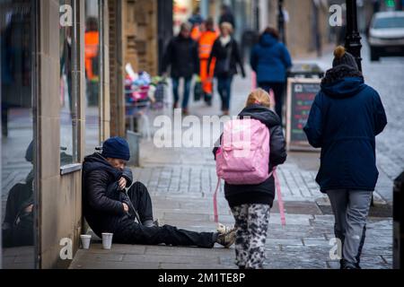 A man begging for money on a town centre shopping street in Halifax, West Yorkshire, UK, as Christmas shoppers pass by. Stock Photo